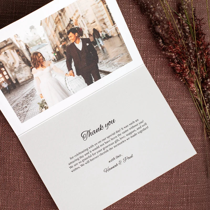 Open folded thank you card with a wedding photo of a couple walking hand in hand down a cobblestone street, above a printed thank you message.