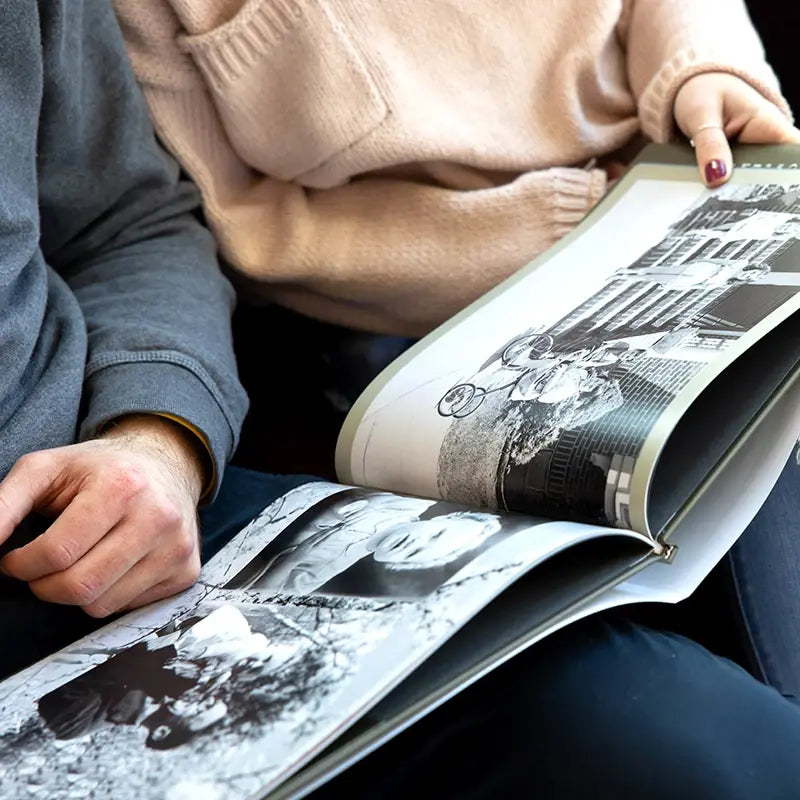 Two people sitting together flipping through an open hardcover photo book displaying black and white photography spreads