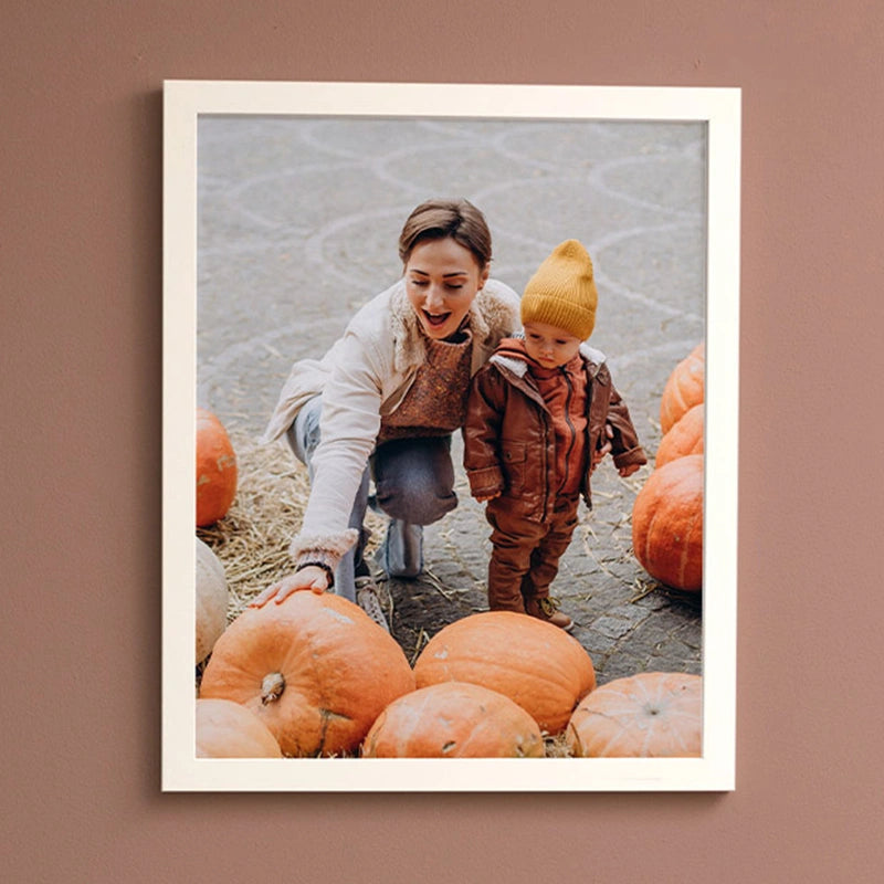 Framed photo print of a mother and toddler in a yellow beanie picking out pumpkins, hanging on a mauve wall.