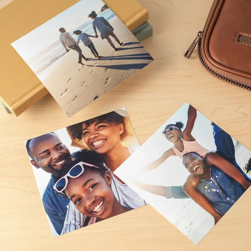 Three photo prints on a wooden surface, featuring a family walking on the beach, a smiling family portrait, and a father giving his daughter a piggyback ride