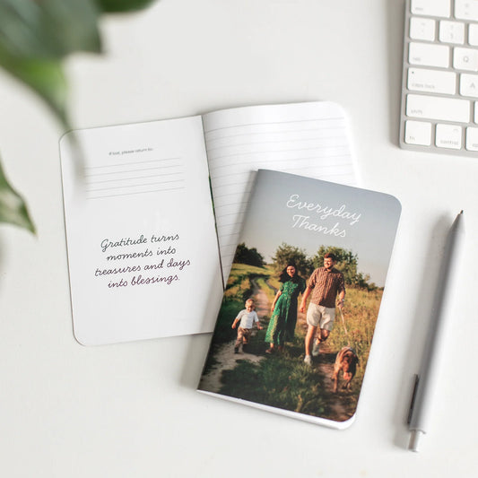 Open memo book displaying a family walking outdoors on the cover titled “Everyday Thanks,” next to a page with printed text.