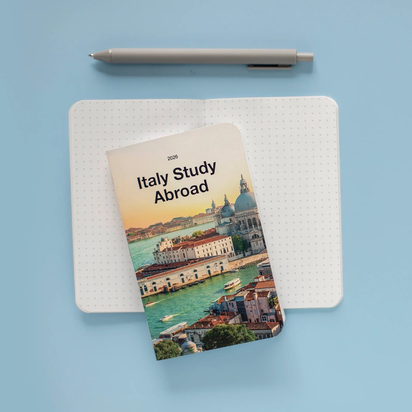 Pocket-sized memo book with an Italy cityscape cover reading “Italy Study Abroad,” placed on open dotted pages with a pen above.