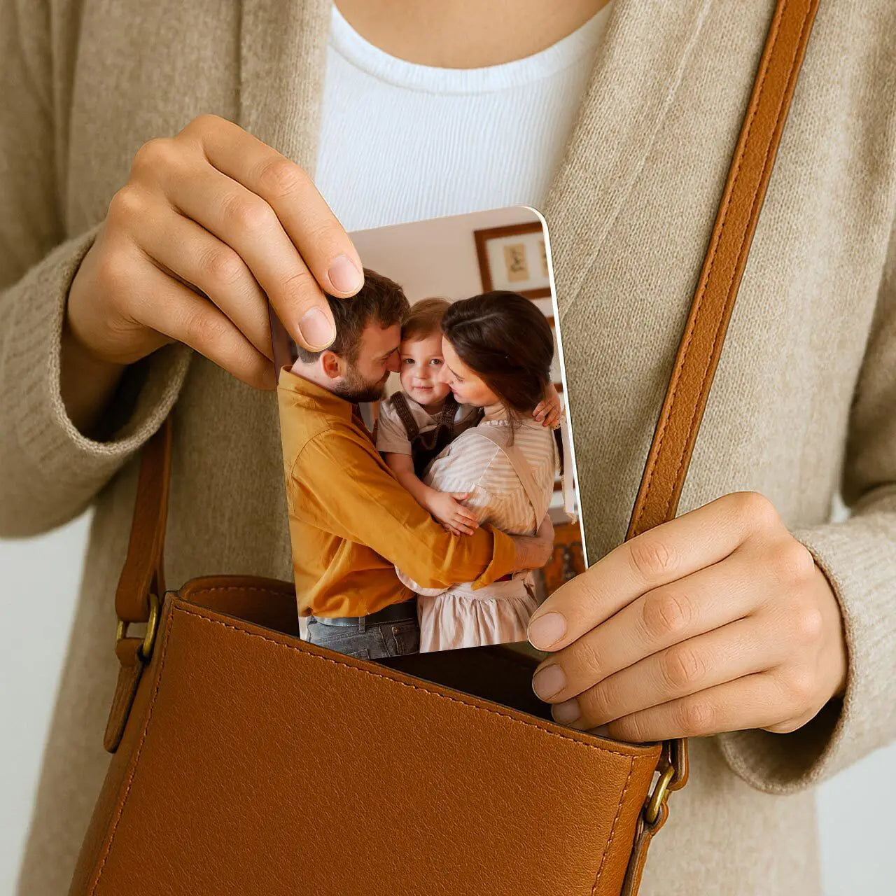 Person placing small custom memo book with rounded corners and family photo cover into brown leather crossbody bag.