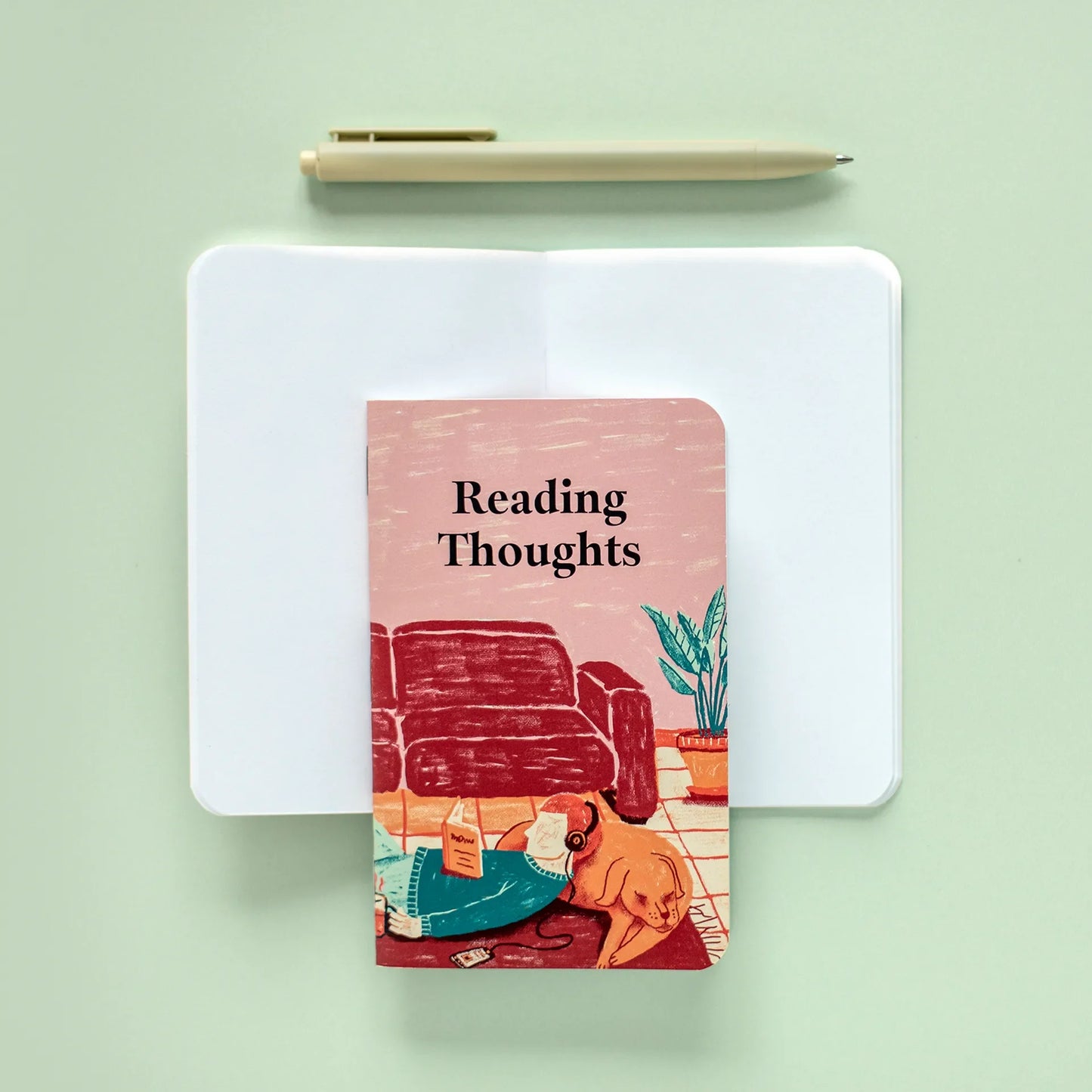 Memo book with illustrated “Reading Thoughts” cover centered on open blank pages, with a pen placed above on a green surface.