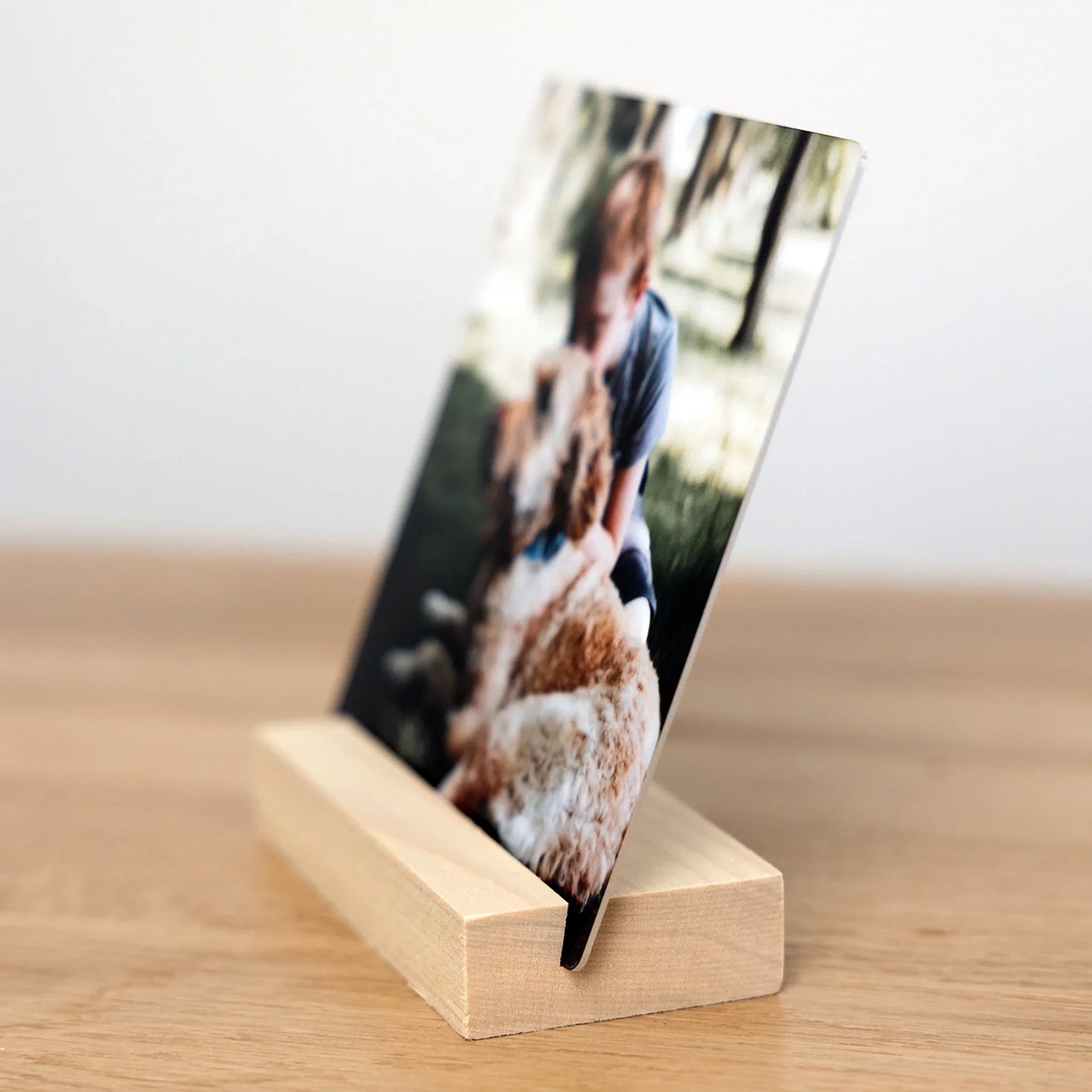 Side view of a metal desk print inserted into a natural wood block stand, showing the slim metal panel and angled display design.
