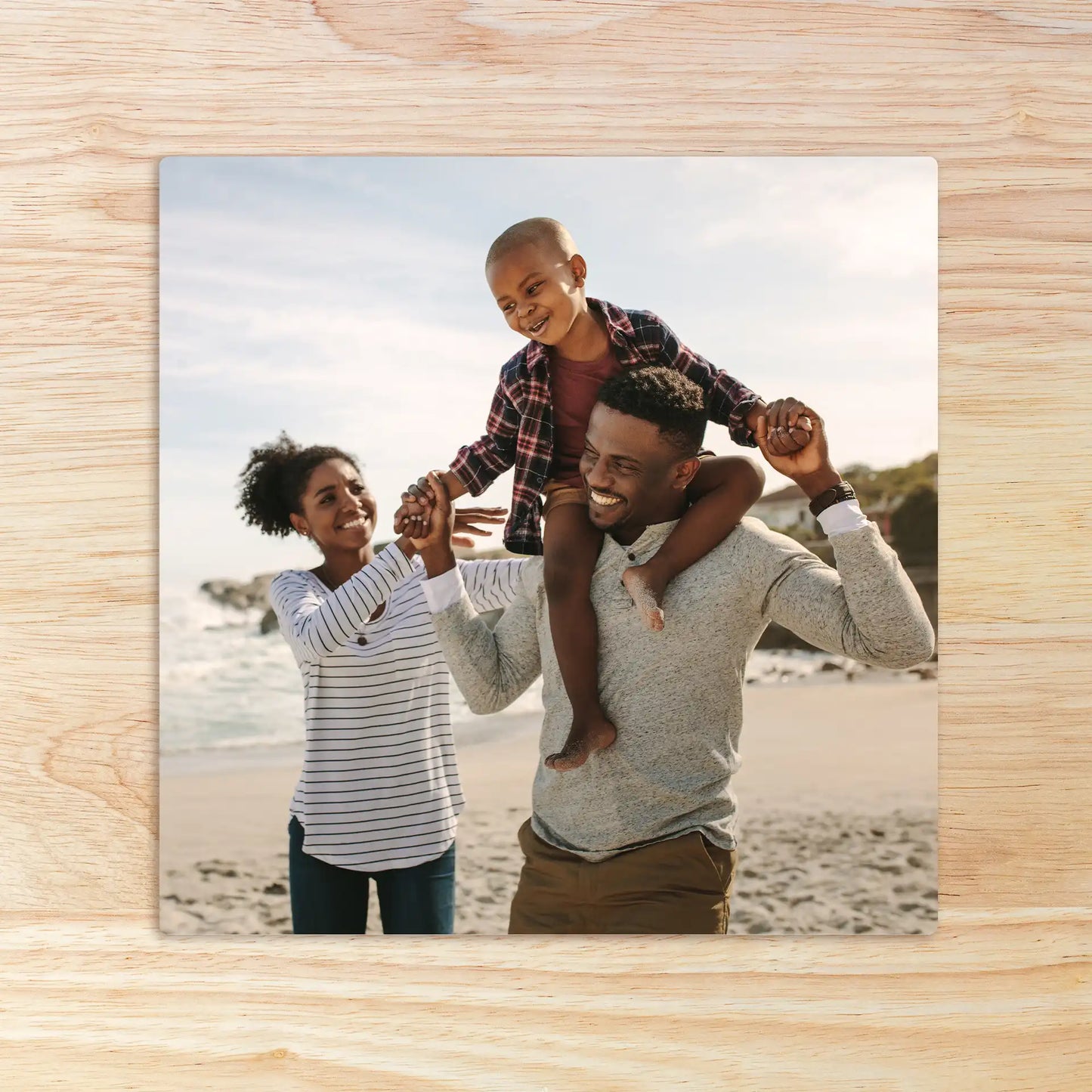 Metal wall decor print of a family at the beach with a child sitting on an adult’s shoulders while another adult holds their hand.
