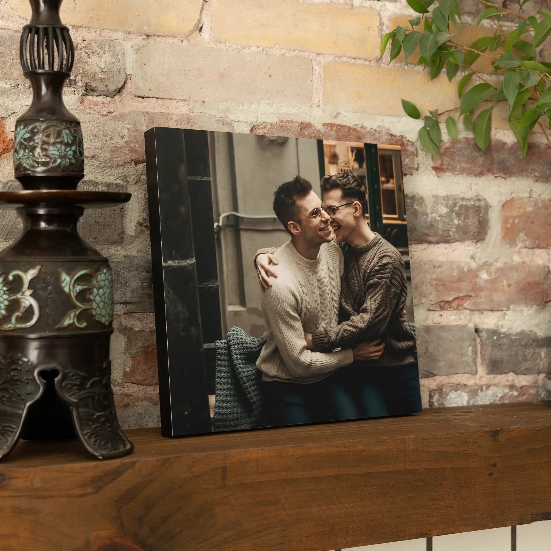 Mounted photo print showing two people embracing and smiling indoors, resting on a wooden shelf against a brick wall.
