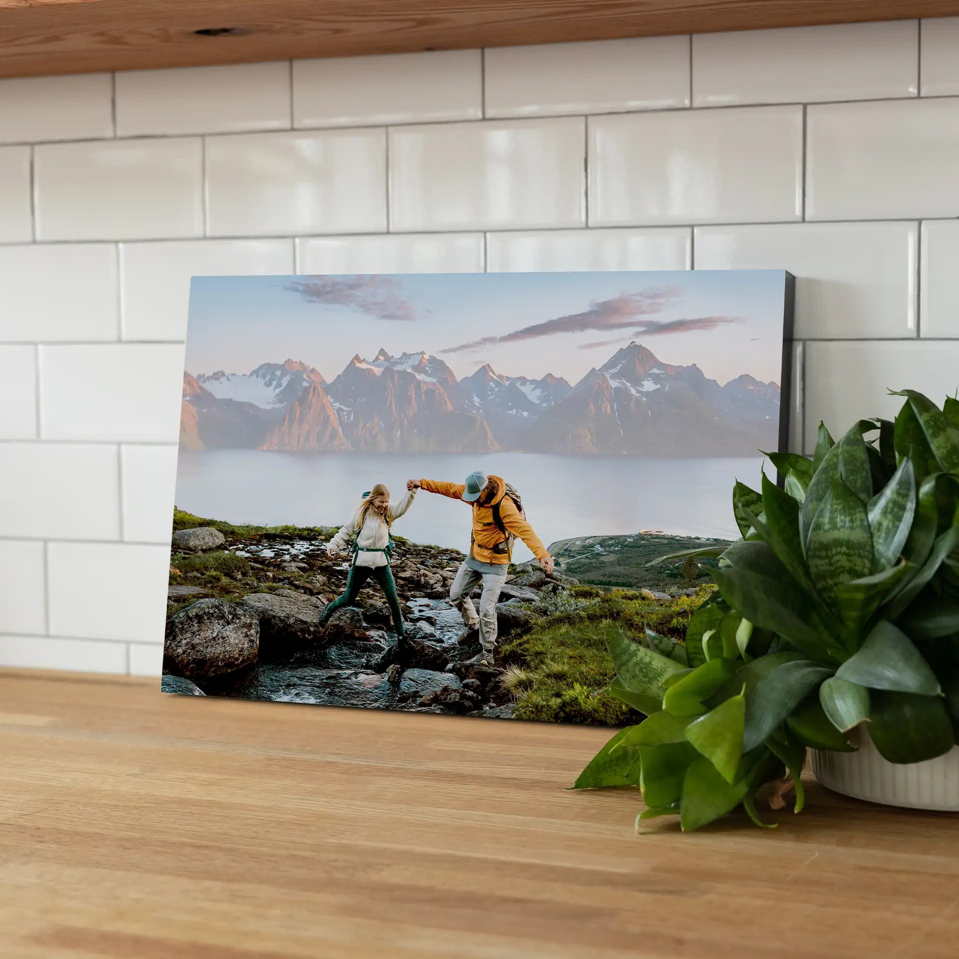 Mounted photo print featuring a couple stepping across rocks near a lake with mountains in the background, displayed on a kitchen countertop.