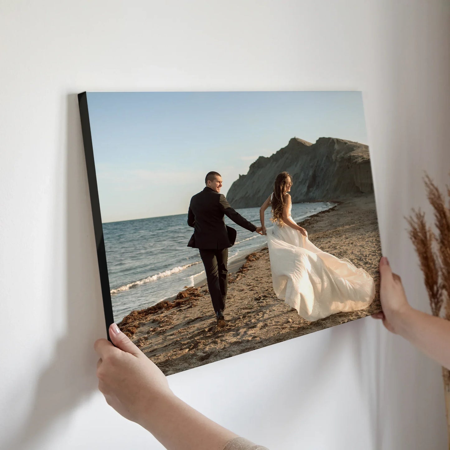 Mounted photo print of a couple holding hands while walking along a sandy beach shoreline, being positioned on a wall.