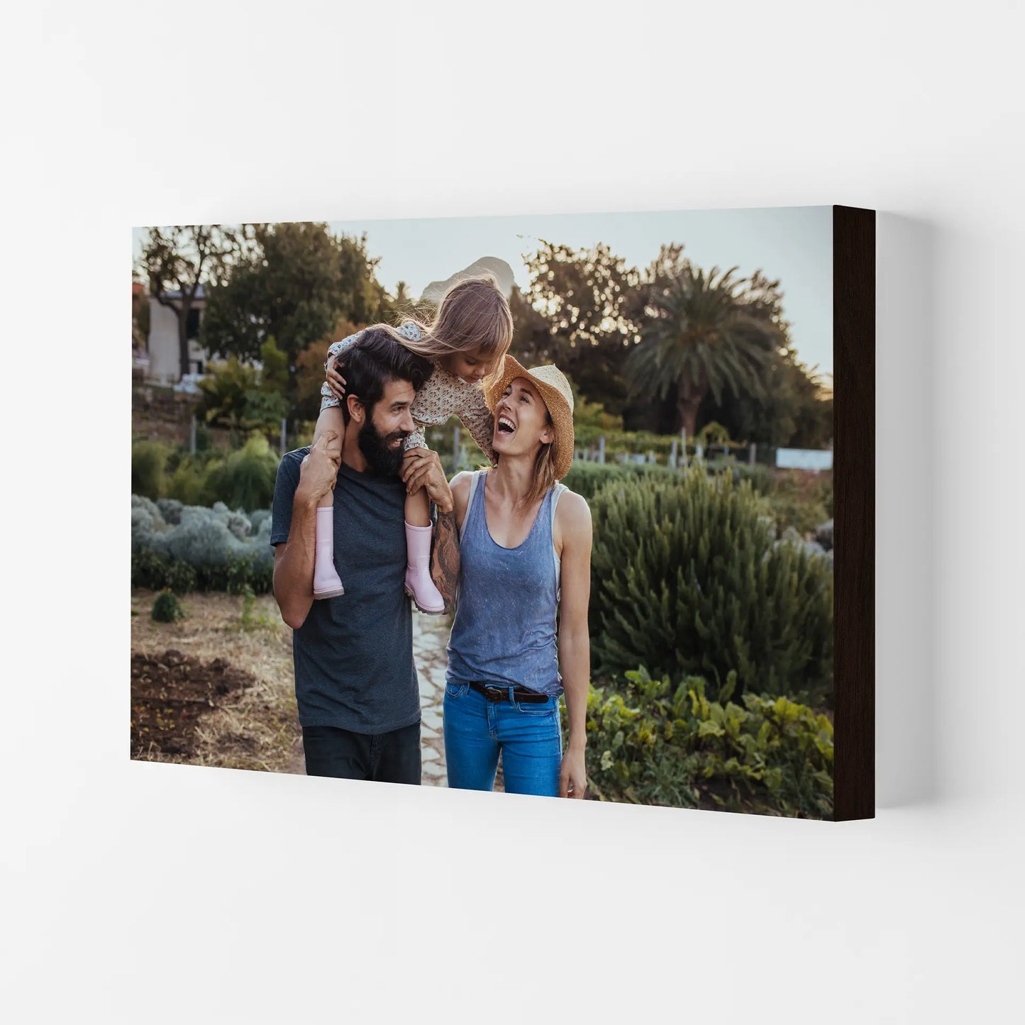 Mounted print featuring parents and child walking through garden, candid moment with greenery background, thick edge profile, displayed on wall.