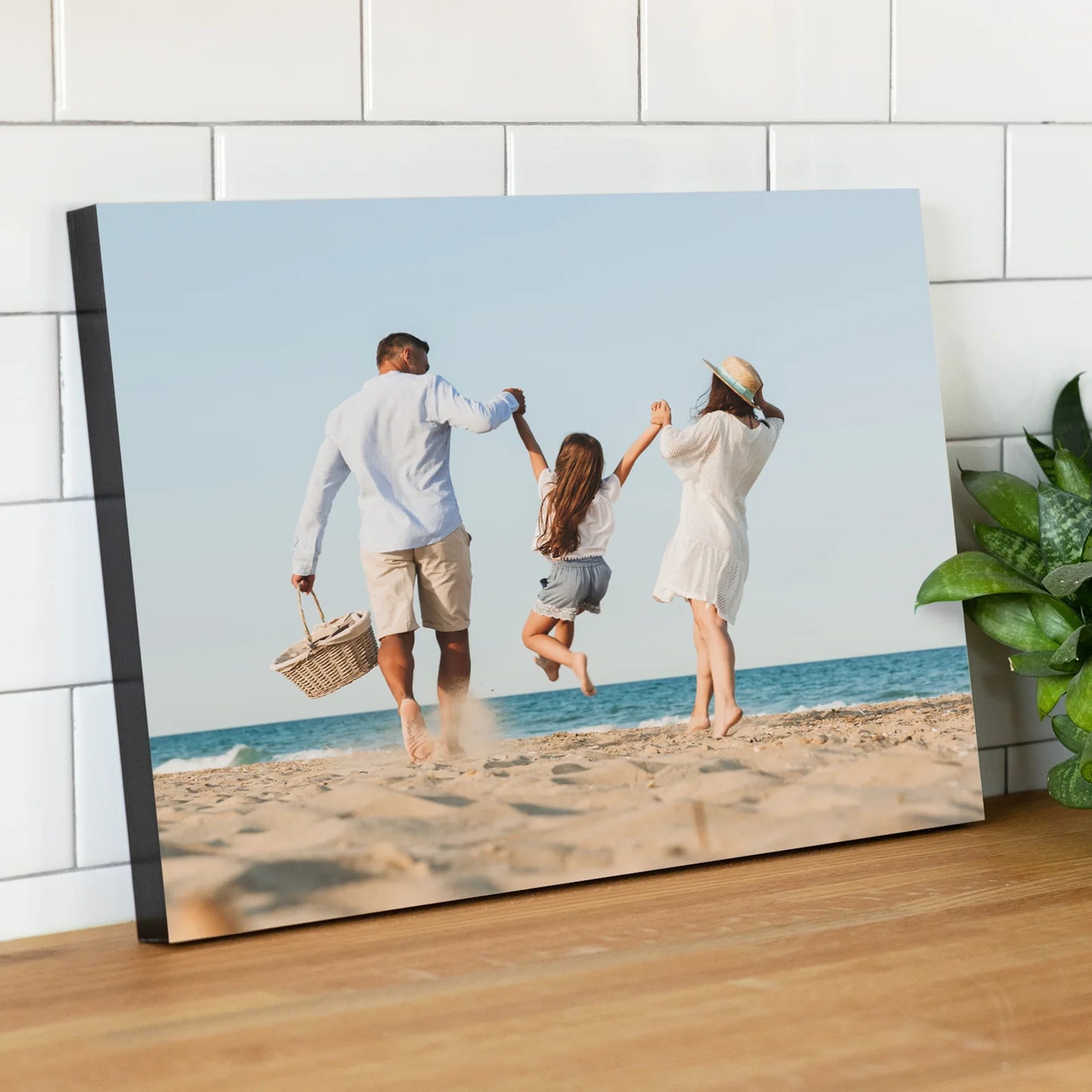 Mounted photo print of two adults and a child running along a sandy beach, displayed on a wooden countertop.