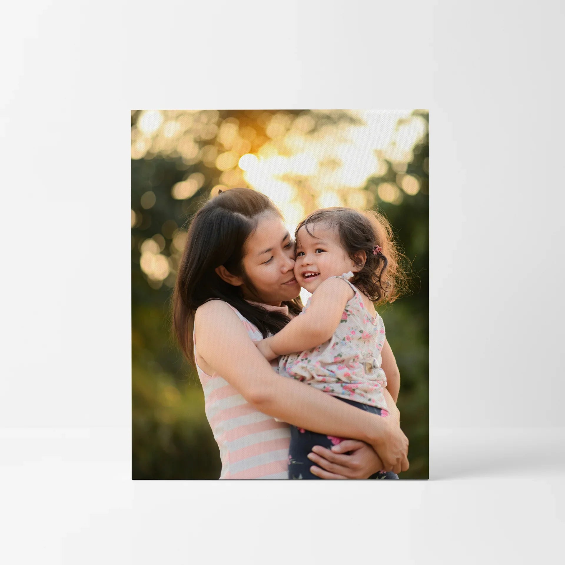 Mounted print with close-up of mother holding young child outdoors, soft sunlight and blurred background, square format, frameless wall display.