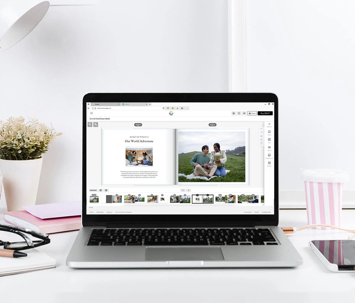 Laptop on a styled desk showing a photo book editor with an open family travel spread and page thumbnails below.