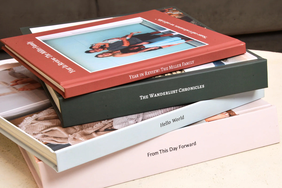 A stack of four custom layflat photo books with personalized covers in terracotta, deep green, light blue and blush.