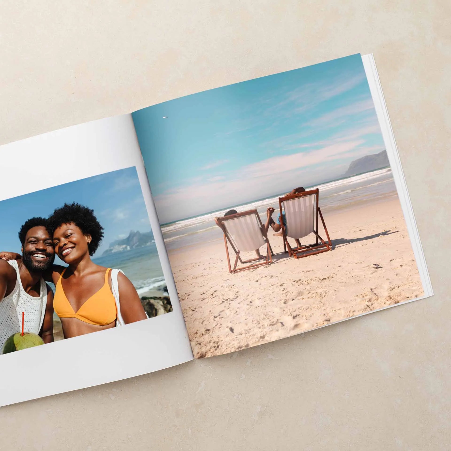 Softcover photo book open to full-page beach image of two people seated in lounge chairs facing ocean, with smaller portrait photo on opposite page.