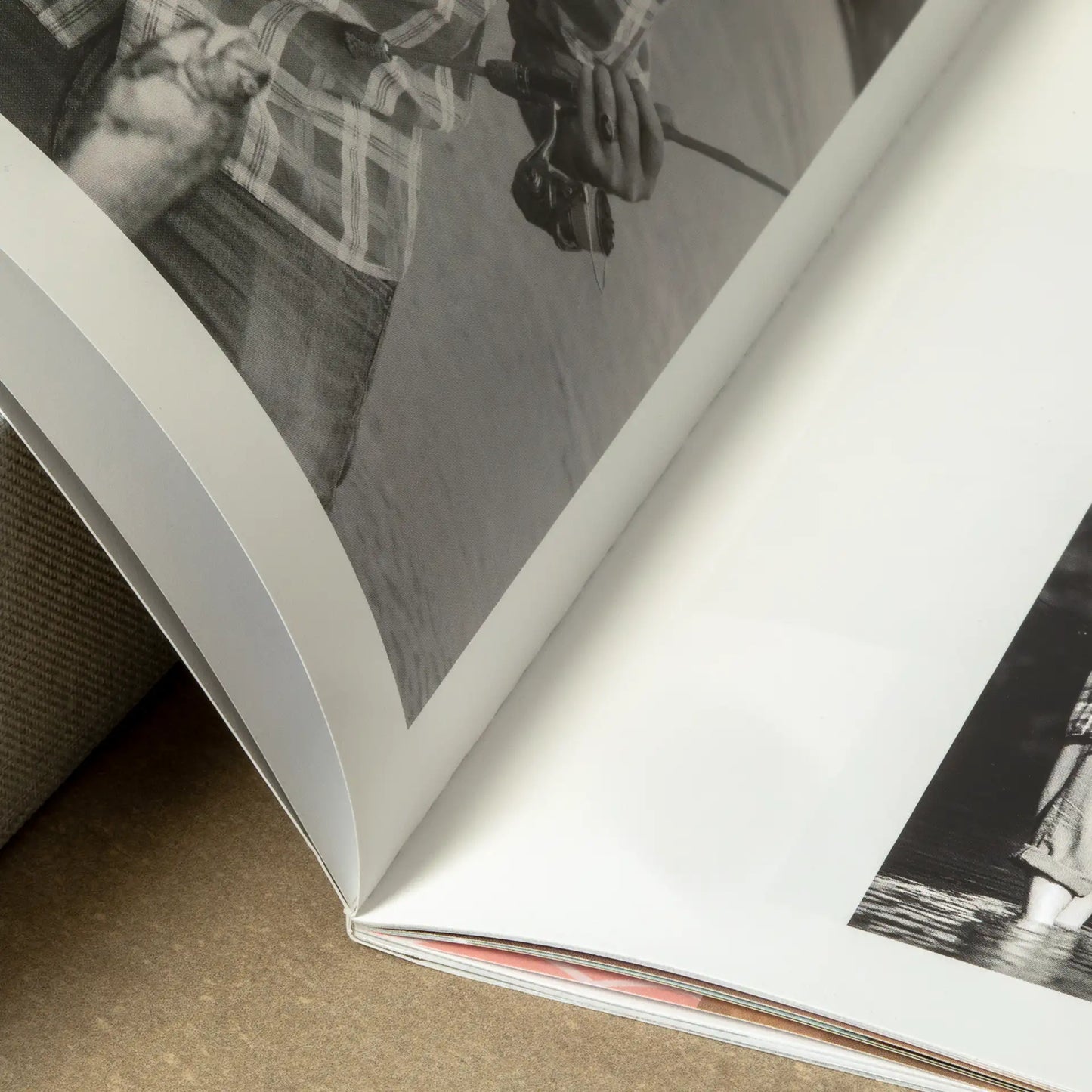 Close-up detail shot of an open softcover photo book showing the flexible spine and smooth paper pages with a black and white fishing photo