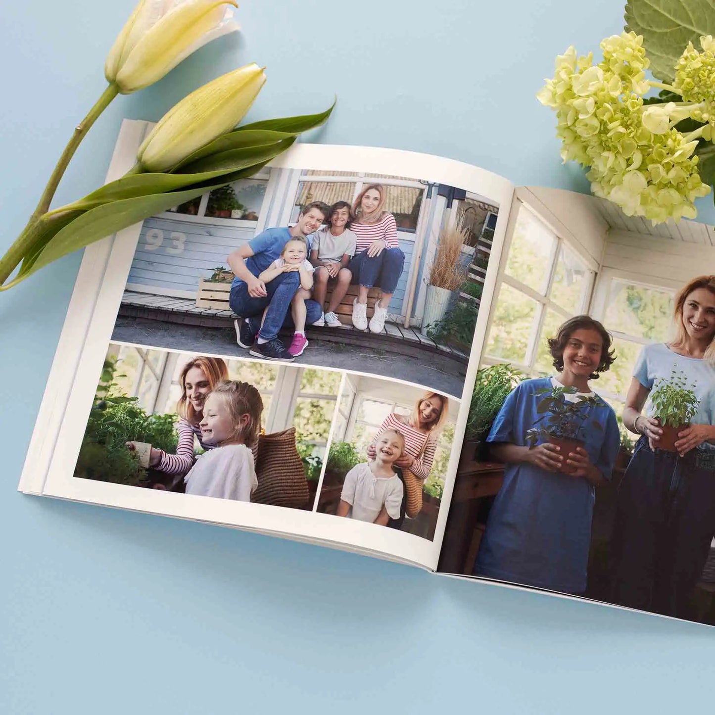 Softcover photo book open to collage layout with family portraits and candid moments, placed on blue background with flowers.