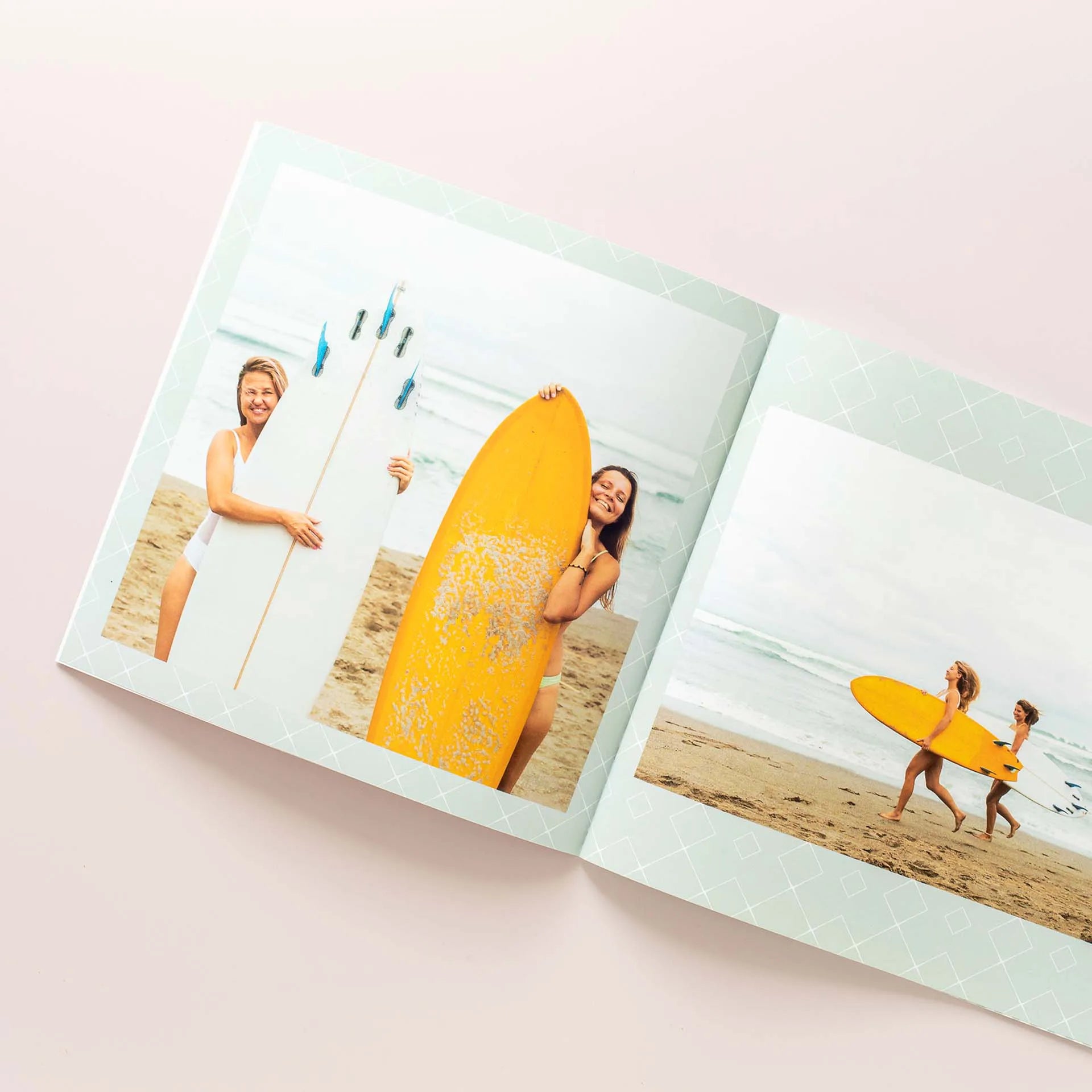 Softcover photo book open to beach layout with people holding surfboards and walking along shoreline, printed on light patterned pages.