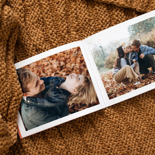 Softcover photo book open to autumn photos of a father and son playing in fallen leaves, and a family embracing outdoors
