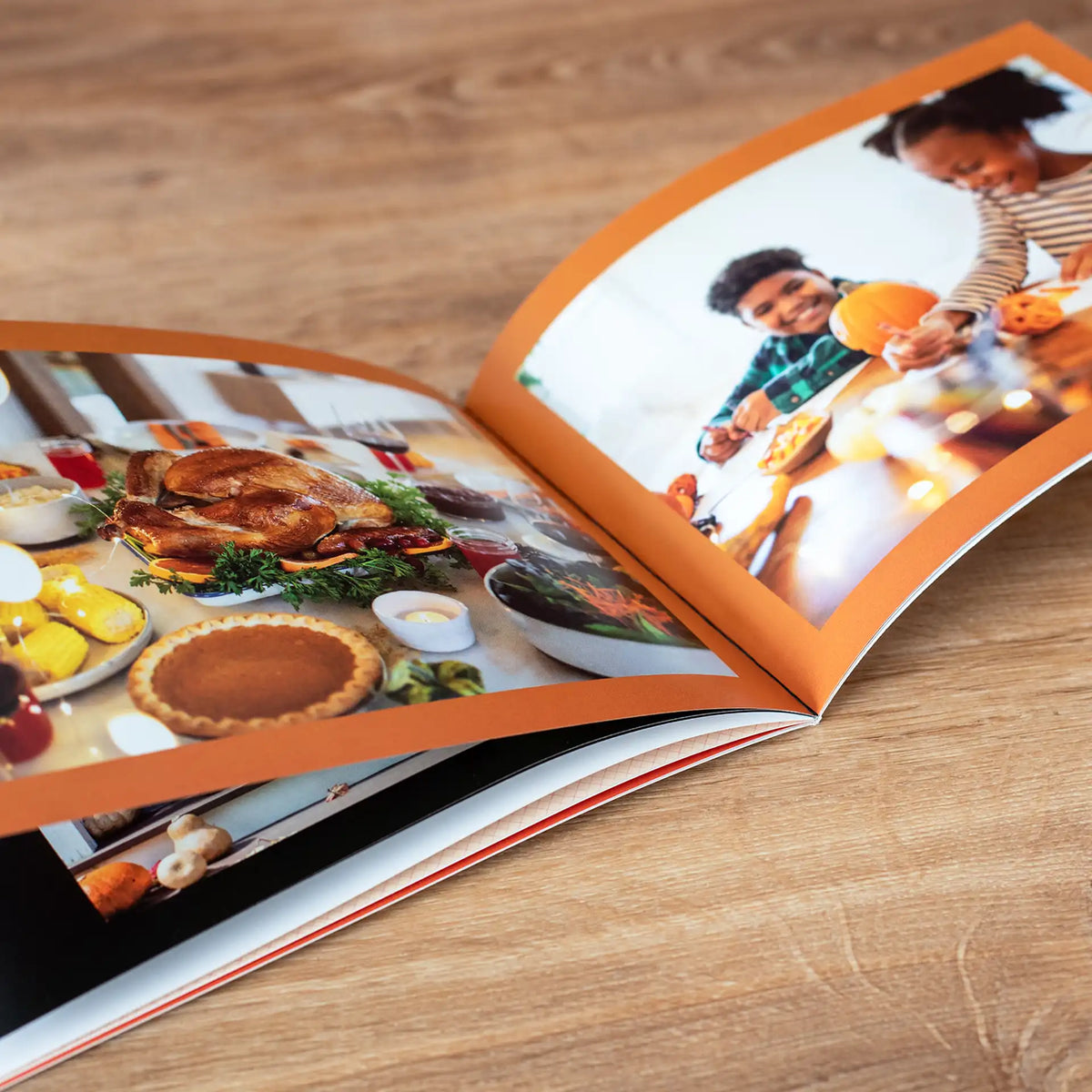 Softcover photo book open to a Thanksgiving spread of turkey and pie, facing a photo of kids helping prepare food in the kitchen.