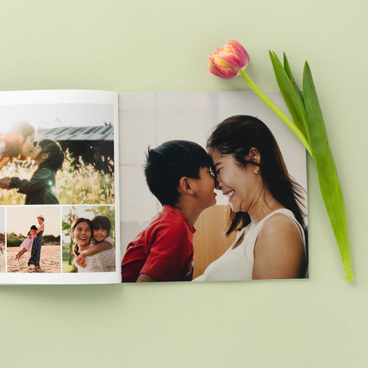 Open softcover photo book featuring a full-page mother and son portrait with smaller family images on the opposite page, styled on a green background with a pink tulip.