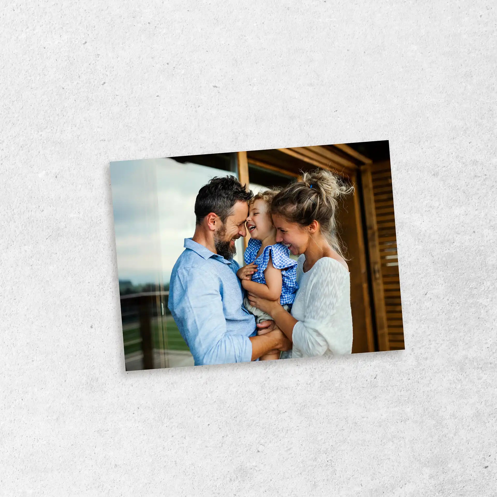 Standard landscape photo print showing a family smiling and holding a child outdoors, displayed against a light textured surface.