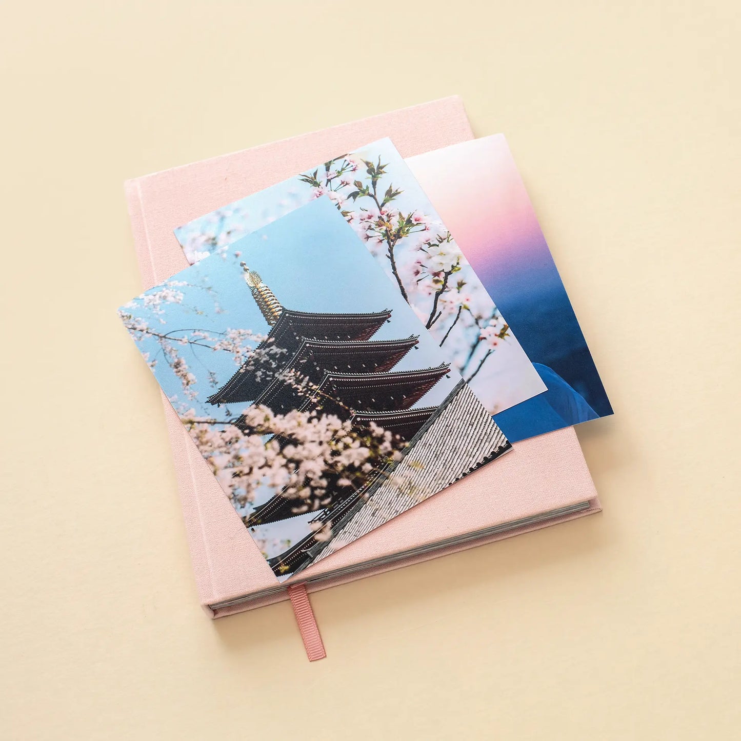Standard photo prints featuring travel scenes placed on a closed linen photo book with ribbon bookmark on a neutral background.