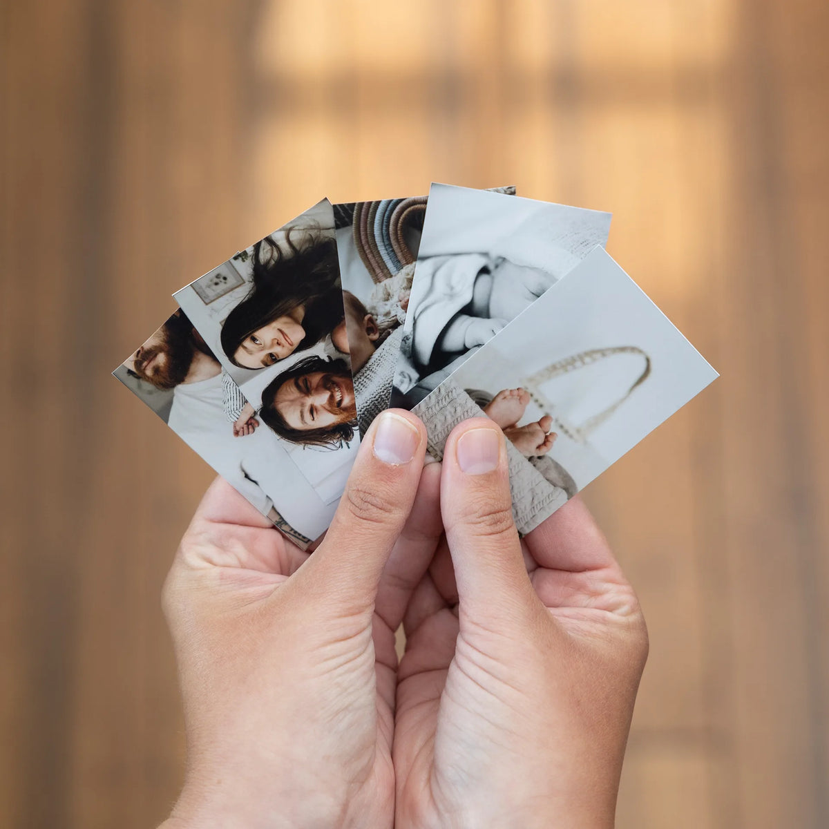 A hand fanning out several small black-and-white standard prints of a family and a newborn baby.