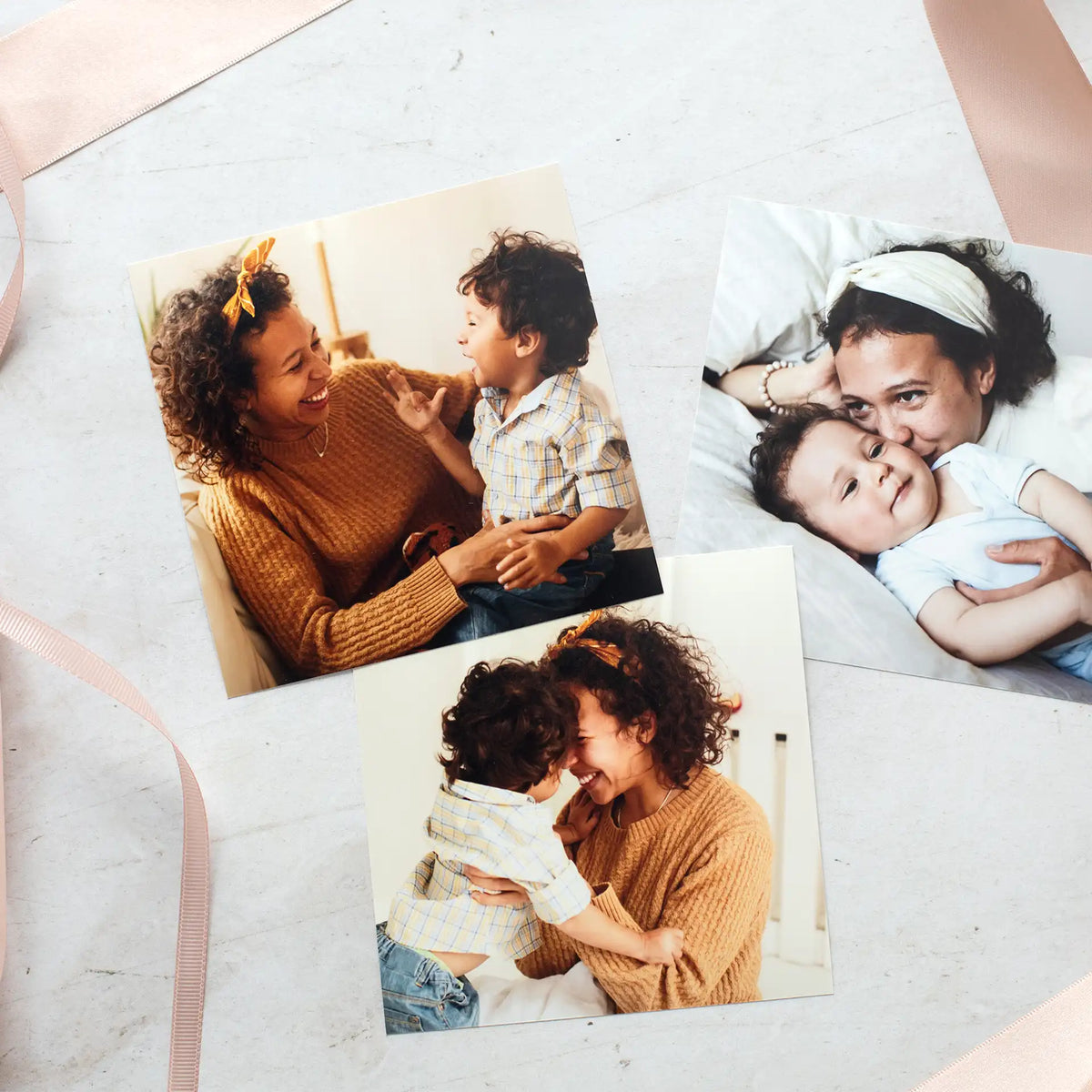 Three loose standard photo prints of a mother and young son laughing together, scattered on a table with ribbon