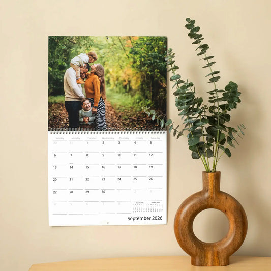 September 2026 wall calendar hanging on a wall, showing a family hugging in an autumn forest above the date grid.