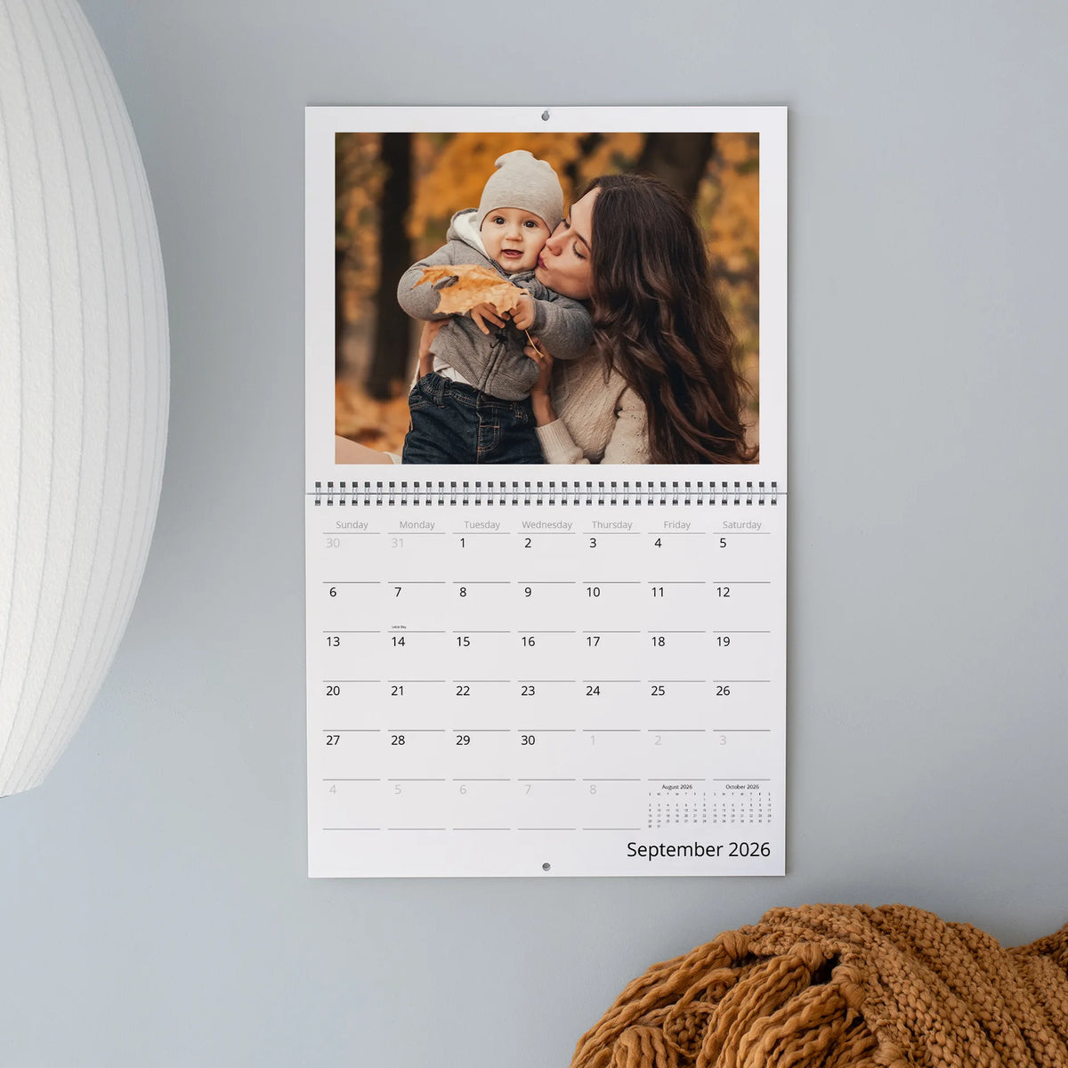 September 2026 wall calendar page with a photo of a mother kissing her toddler in a autumn forest, above the monthly grid.