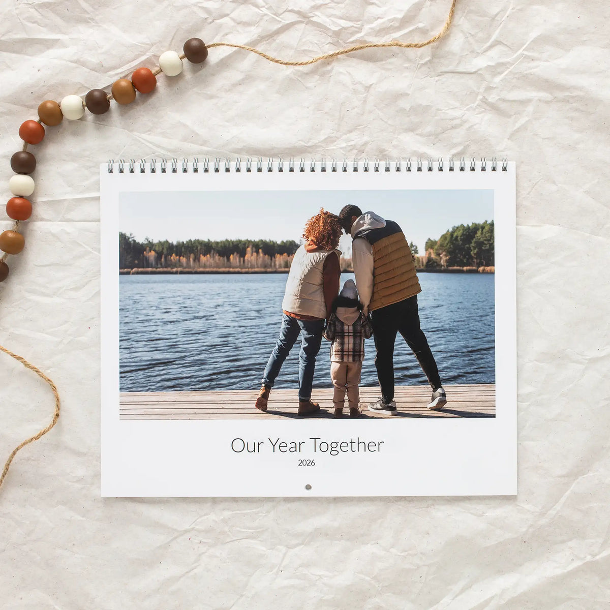 Spiral-bound wall calendar cover titled 'Our Year Together 2026,' featuring a family standing on a lake dock.