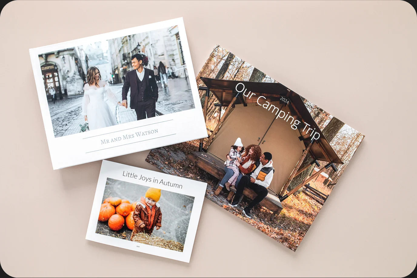Three printed photo books arranged on a neutral surface, featuring wedding, camping, and autumn-themed covers with custom titles and images.