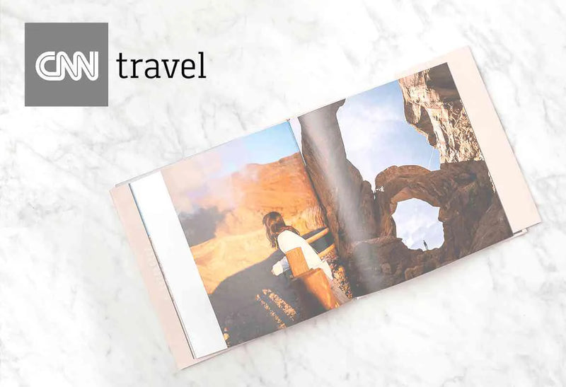 Open hardcover photo book displaying a travel landscape spread with a person overlooking a canyon, with CNN travel logo overlay in the top left corner.