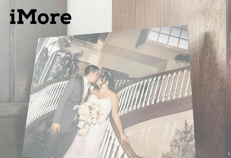 Printed wedding photograph of a couple kissing on a curved staircase inside an elegant building with railings, featuring iMore logo.