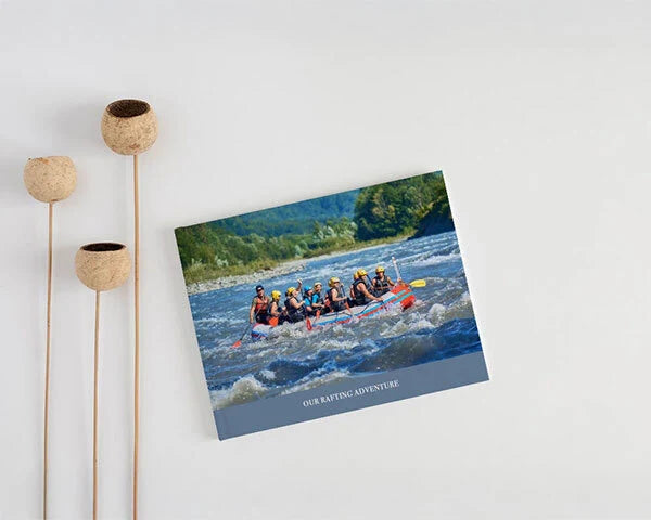 Photo book featuring rafting group navigating river rapids with caption “Our Rafting Adventure,” displayed on neutral surface beside decorative stems.