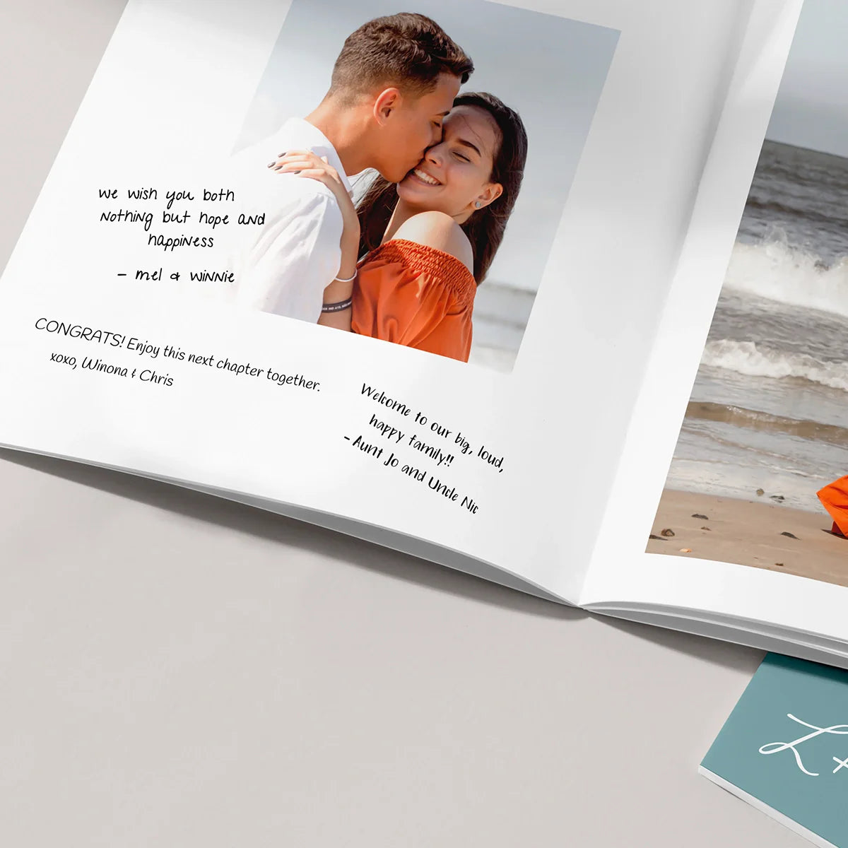Open softcover photo book displaying engagement portrait with handwritten congratulatory messages around the photo.