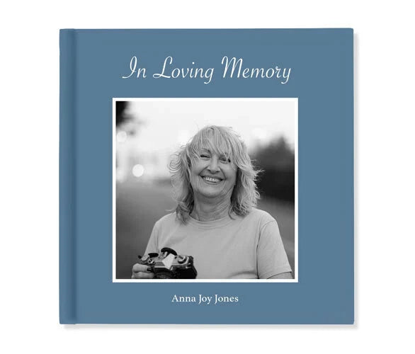 Softcover photo book cover with blue background, centered black-and-white portrait, and “In Loving Memory” title above name text.
