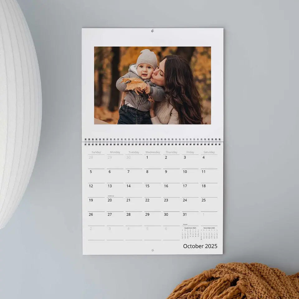 Wall calendar opened up to October 2025 with a photo of a woman and child on a gray wall.