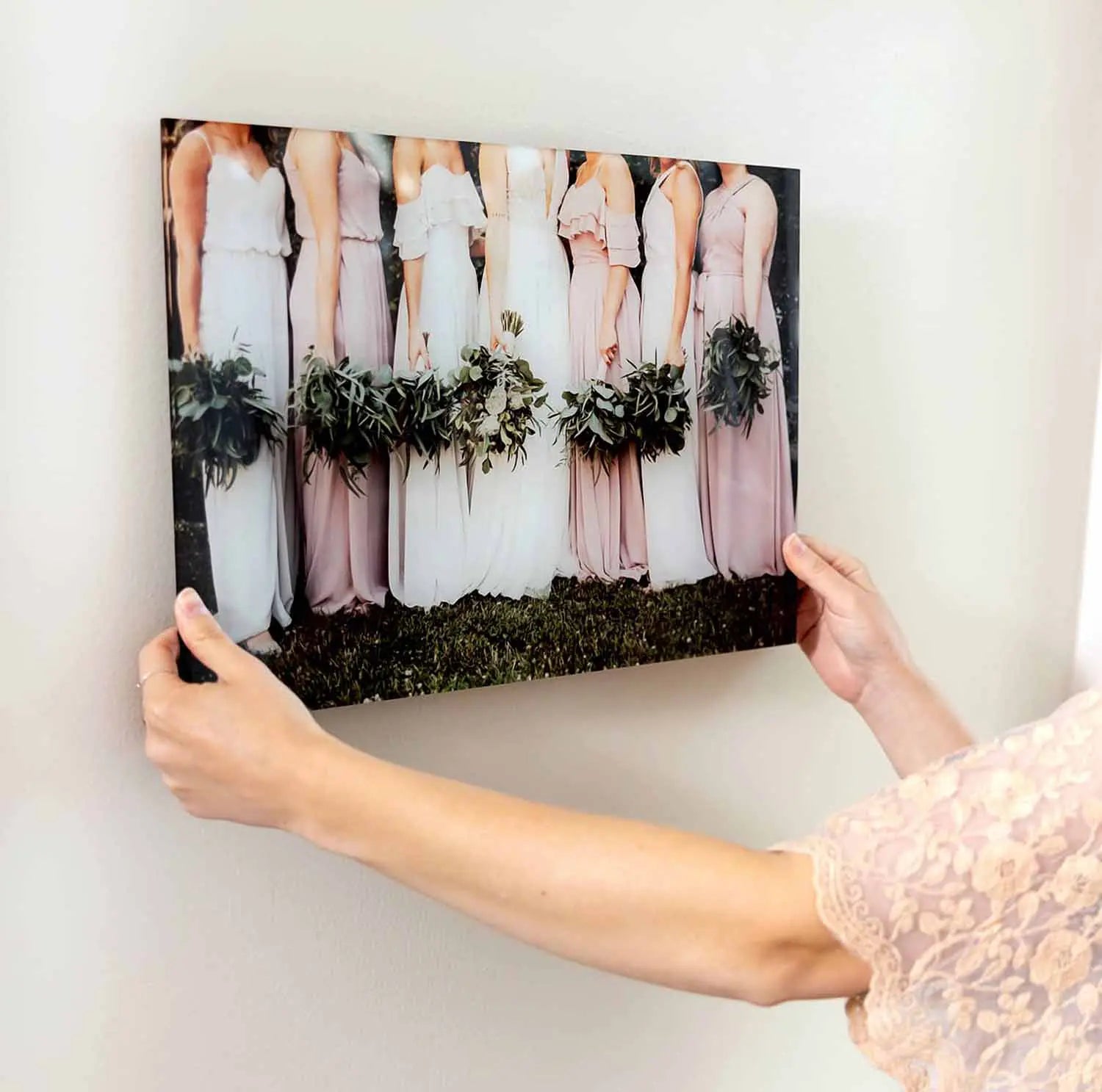 Acrylic wall print of bridesmaids in blush dresses holding green bouquets, being positioned on a light-colored wall.
