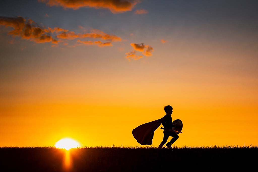 childs silhouette during sunset wearing super hero costume