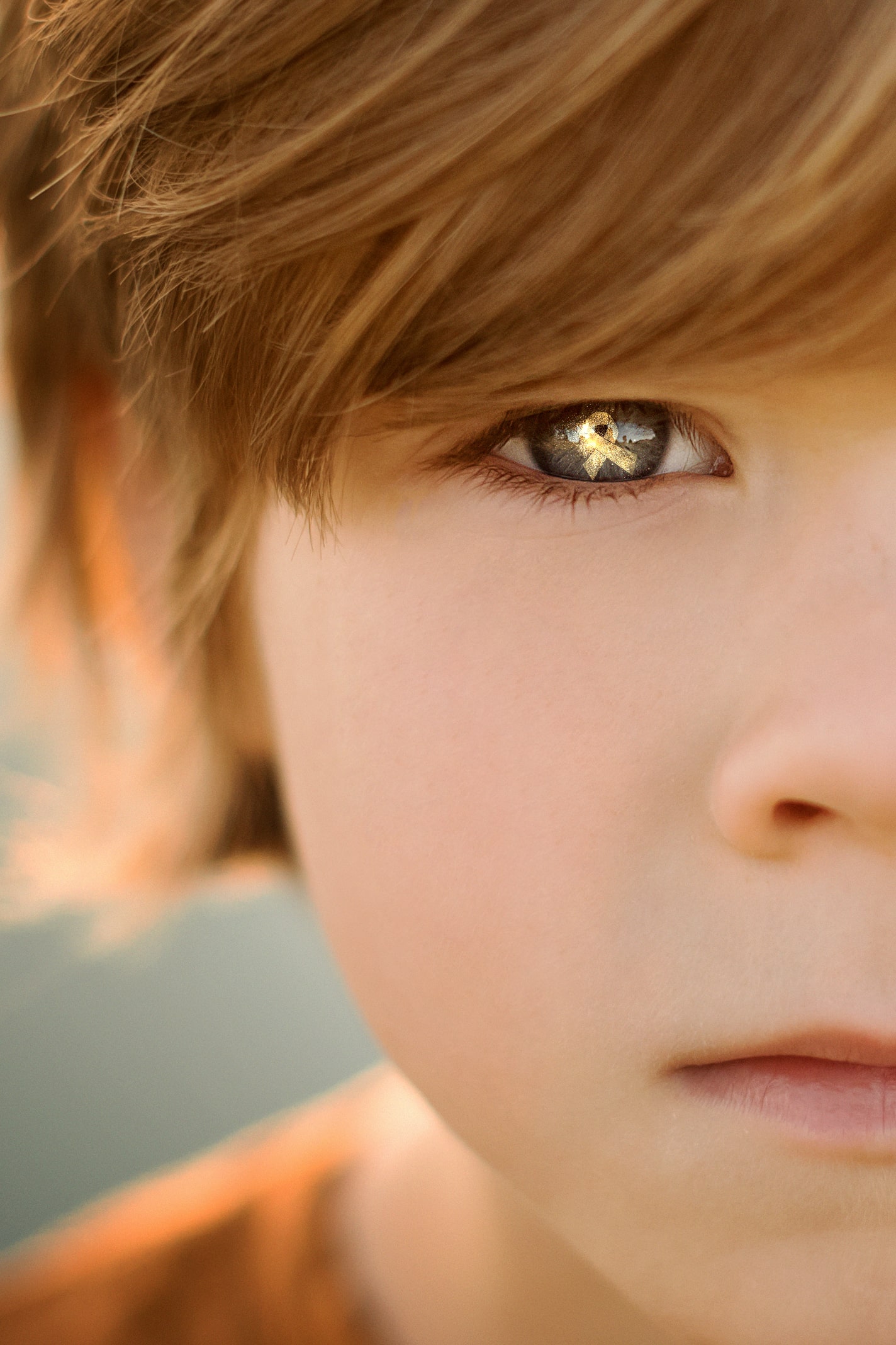 close up of child with blonde hair with cancer ribbon in eye