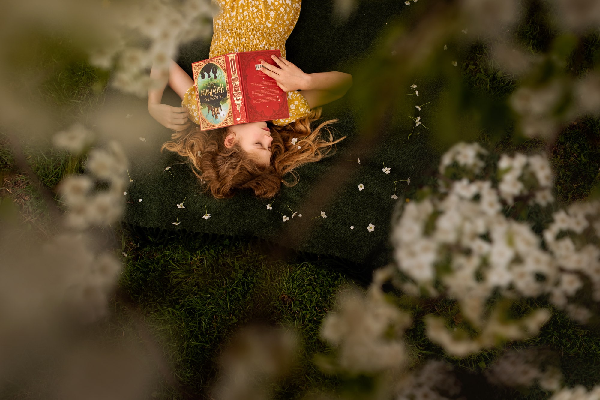 girl laying in grass with harry potter book and flowers in her hair