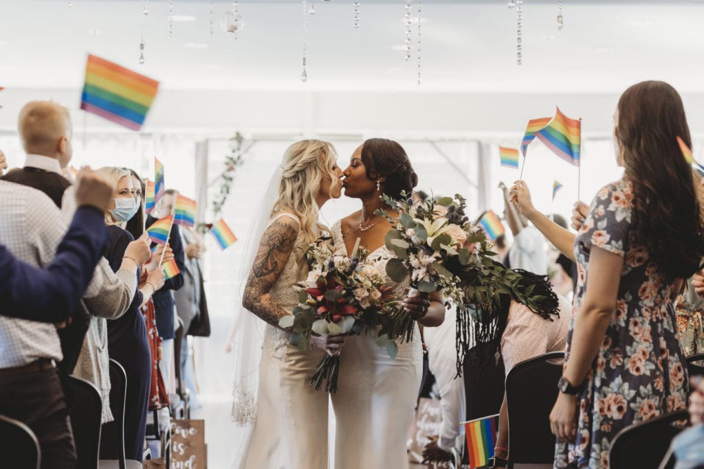 lesbian interracial couple kissing walking down the aisle surrounded by pride flags