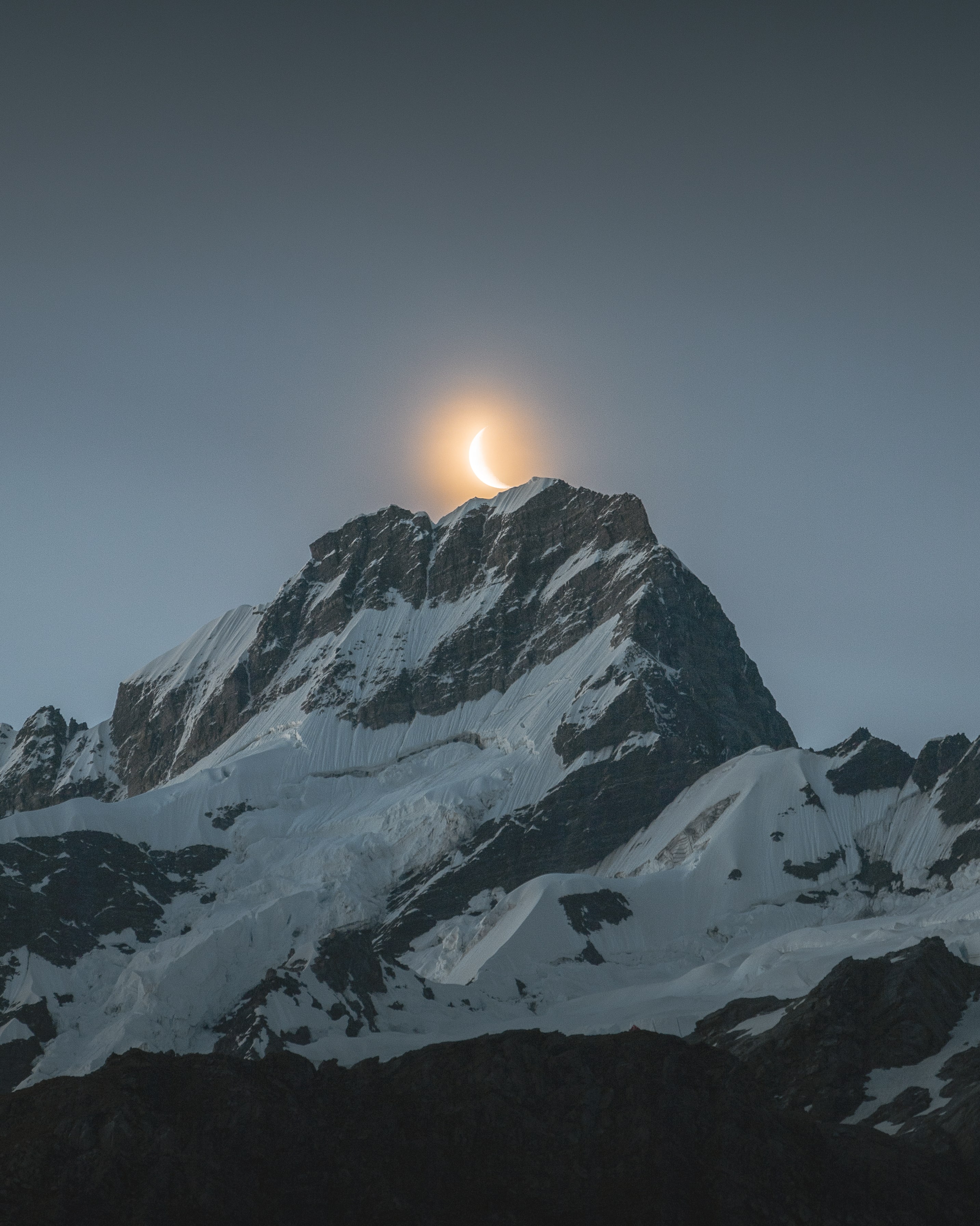 crescent moon glowing behind mountain