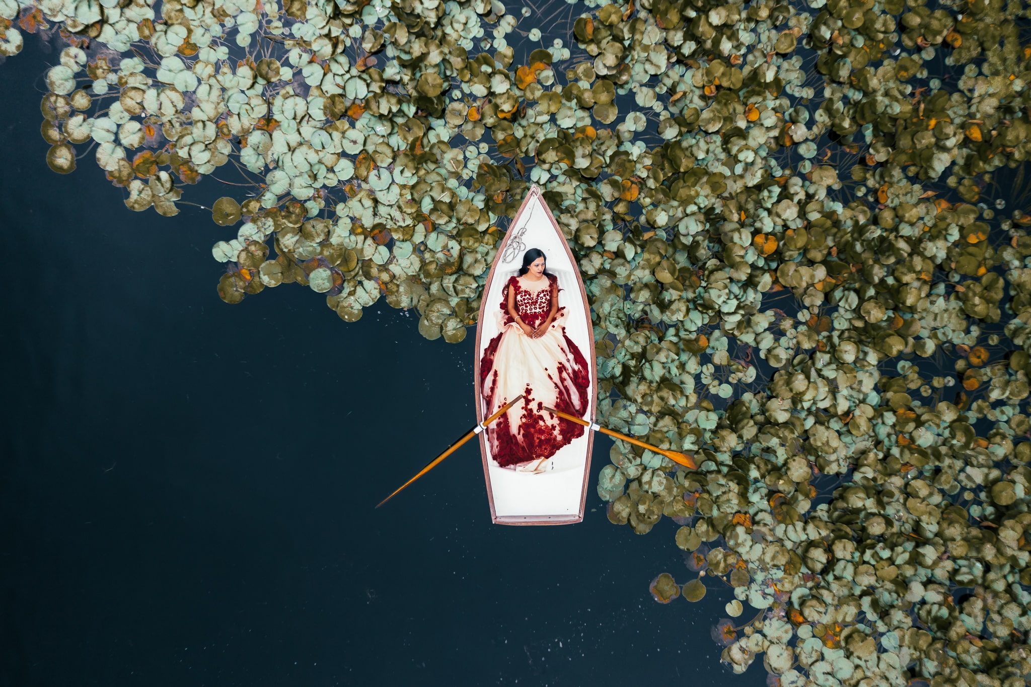 overhead drone shot of girl laying on a boat in a pond surrounded by lily pads 