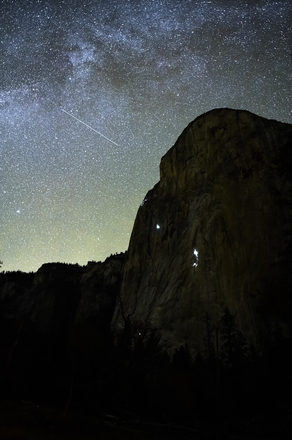 starry night sky and climbers climbing up the side of a mountain