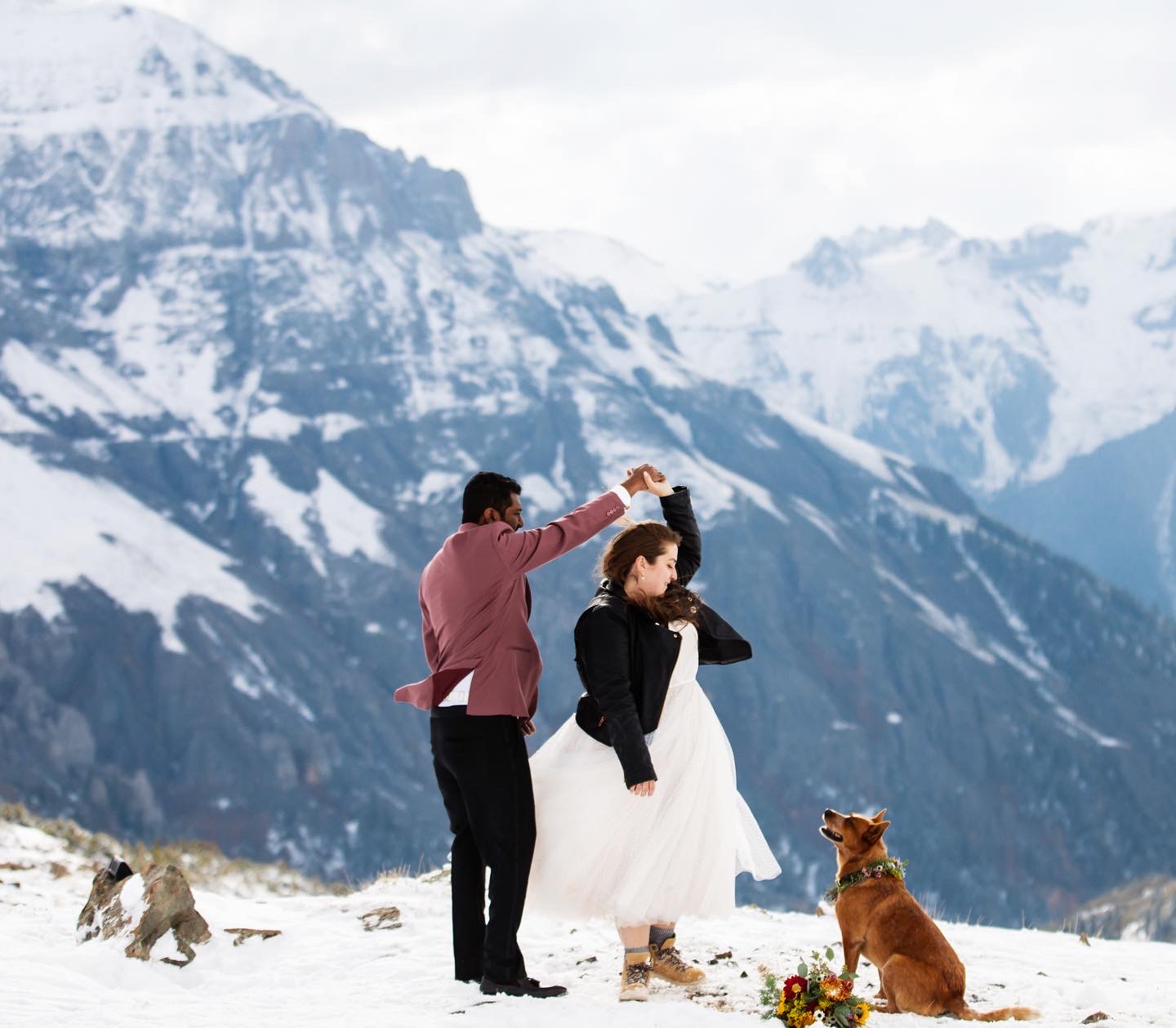 couple in formal outfits dancing on top of snowy mountains