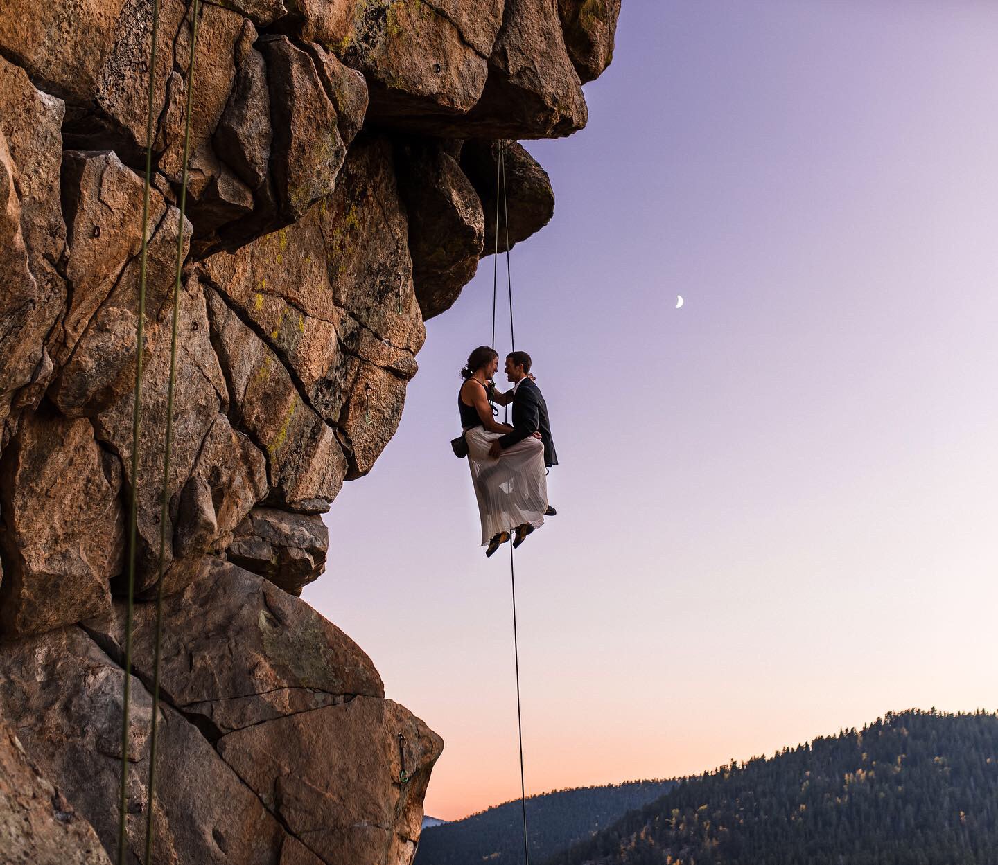 couple suspended in midair holding each other at sunset