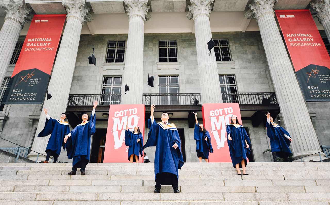 college graduate throwing hats wearing blue gowns